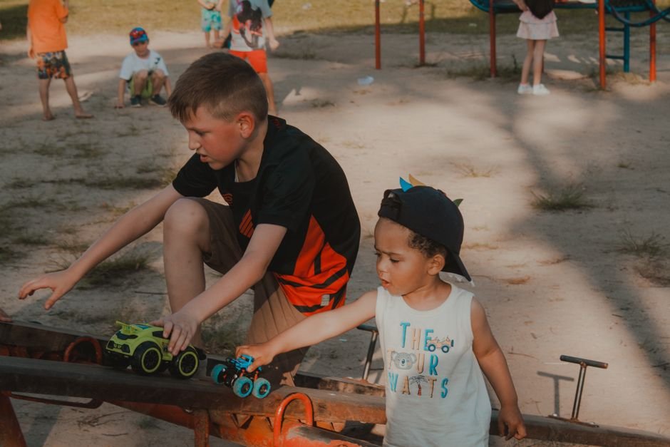 Vaikai džiaugsmingai žaidžia su mašinėlėmis saulėtoje, kruopščiai įrengtoje aikštelėje